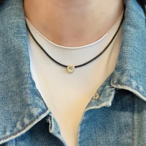 Nahaufnahme einer minimalistischen schwarzen Kordelkette mit goldenem Herzanhänger und Kristall.