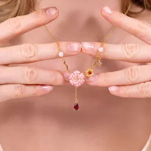 Vergulde bloemenketting met roze geëmailleerde bloem, parels en rode druppelhangertje.