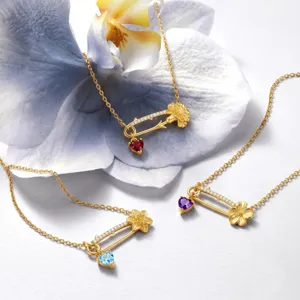 Gros plan sur le collier épingle de sûreté doré avec pierre de naissance cœur et pendentif fleur.