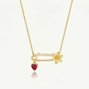 Vue détaillée du collier épingle de sûreté doré avec fleur et pendentif en cristal cœur rouge.