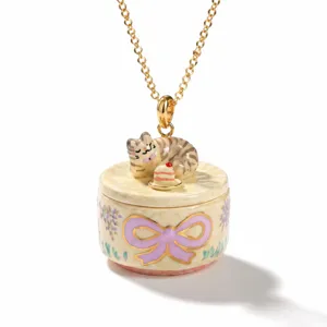 Close-up of a cute sleeping cat and miniature cake pendant necklace with enamel bow design.