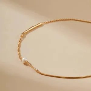 Detailopname van het minimalistische vergulde slangenketting- en parelkettingontwerp.