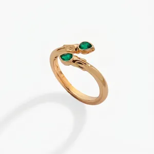 Primer plano de un elegante anillo de serpiente dorado de dos cabezas con piedras de circonita verde.