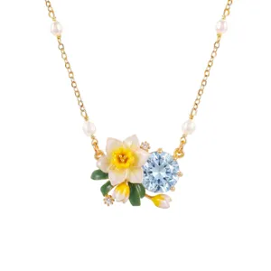 Close-up detail view of gold chain necklace featuring pearl accents, enamel daffodil and blue crystal.