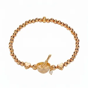 Gros plan sur le bracelet de perles dorées avec un charm de bol de cuisson et des perles en cœur.