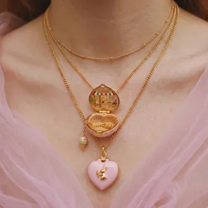 Collier multicouche doré délicat avec médaillon cœur en émail rose et mini-scène de boutique.