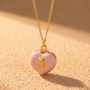 Gros plan détaillé du collier pendentif cœur rose avec un chat doré buvant du thé.