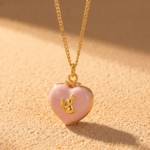 Gros plan d'un joli collier doré avec un médaillon cœur rose et pendentif lapin.