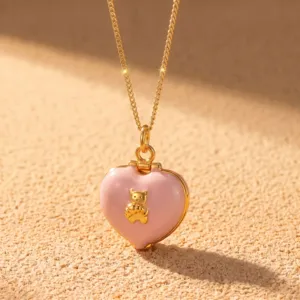 Collier chaîne dorée avec pendentif médaillon cœur rose et détail d'un petit ours doré.