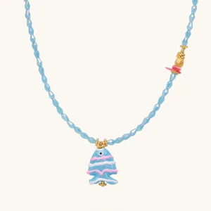 Close up view of the blue beaded necklace featuring a cute fish pendant and gold pineapple charm