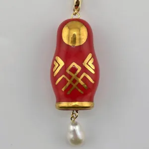 Gros plan détaillé du pendentif poupée russe rouge avec motif doré et perle.