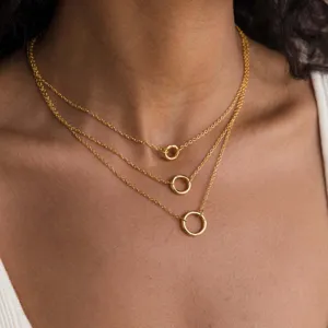 Dettaglio collana a strati dorata con tre catene delicate e ciondoli circolari.