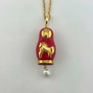 Gros plan d'un collier poupée russe rouge vintage avec cheval doré et perle.