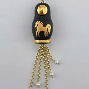 Détail en gros plan du pendentif poupée russe rétro avec motif de cheval doré et chaînes pendantes.