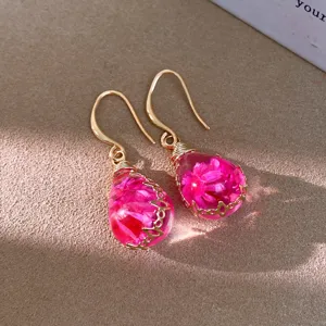 Close-up detail of resin flower teardrop earrings with gold hooks and pink dried blooms.
