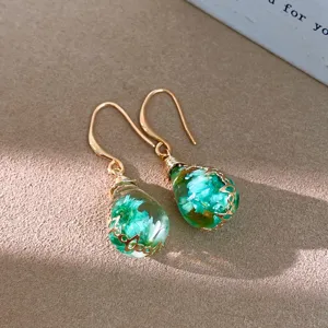 Detail view of bohemian resin teardrop earrings featuring dried green flowers inside.