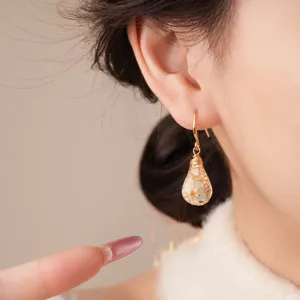 Close-up detail shot of bohemian resin dried flower teardrop earrings worn on ear.