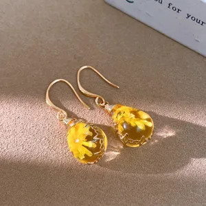 Close-up of golden teardrop resin earrings featuring delicate yellow dried flowers inside.