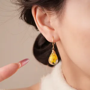 Closeup of bohemian resin teardrop earrings featuring a real yellow dried flower design.