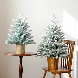 Vista dettagliata del mini albero di Natale innevato in vaso dorato su tavolo di legno.