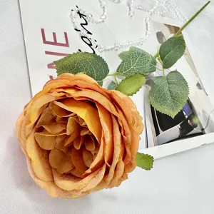 Detailed close-up shot of an artificial orange Austin rose flower with green leaves for home decor.