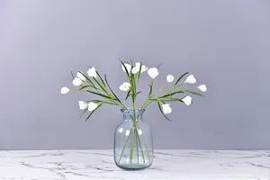 Artificial white crocus flowers in clear blue glass vase for home wedding table decor.