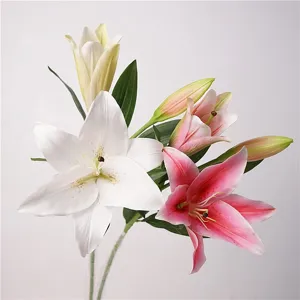 Close-up detail of artificial lily flowers with realistic petals, buds, and green leaves.