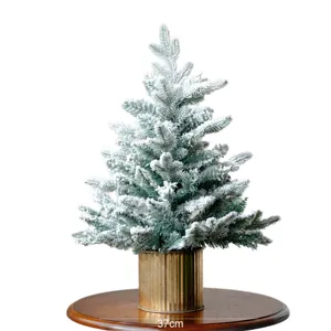 Albero di Natale artificiale innevato da tavolo con vaso dorato per decorazioni festive.