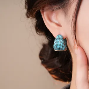 Dettaglio orecchino a goccia in zircone colorato turchese con micro-pavé di pietre scintillanti.