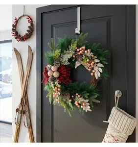 Christmas wreath with pine branches, pinecones, and red-black plaid bow for door decor.