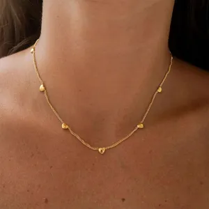 Close-up detail of a delicate gold chain necklace featuring multiple small heart charms.