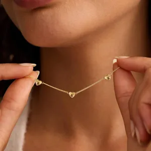 Detail shot of a delicate gold-tone clavicle chain featuring three small heart pendants.