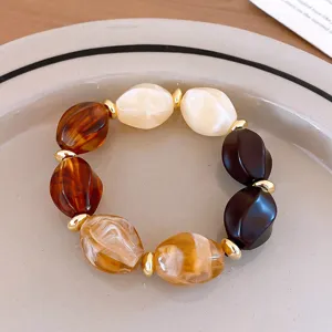 Close-up detail shot of chunky geometric acrylic resin beaded bracelet in amber and cream tones.
