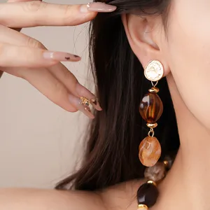 Close-up detail of statement drop earrings featuring resin beads and textured gold metal.
