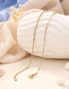 Delicate gold-tone anklet detail view featuring dainty ball charms and lobster clasp on shell prop.
