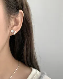 Close-up detail of silver star pearl stud earrings worn on ear, minimal Korean style.