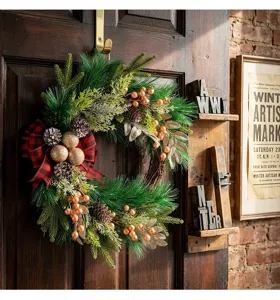 Christmas wreath detail shot featuring pine branches, pinecones, gold berries, and a plaid bow.