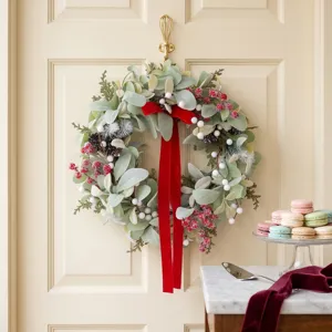 Christmas artificial wreath with red velvet bow, green foliage and berries for holiday decor.
