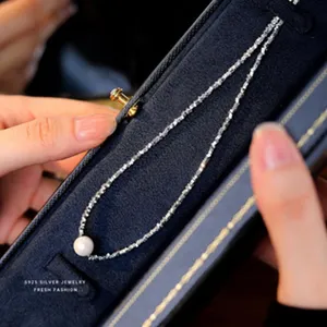 Gedetailleerde close-up van een delicate zilveren ketting met een elegante parelhangertje.
