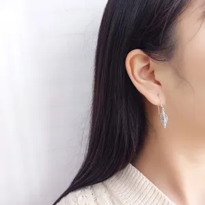 Close-up detail shot of sterling silver leaf hook earrings worn on ear, elegant simple design.