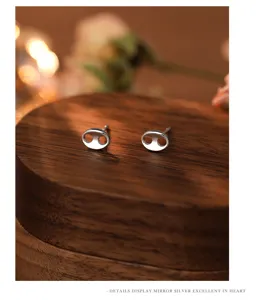 Close-up view of minimalist sterling silver pig nose stud earrings on wood display.