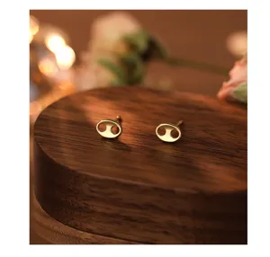 Close-up detail shot of minimalist gold pig nose stud earrings on wood block.