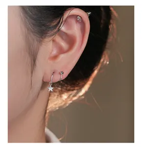 Nahaufnahme von Sterling Silber Stern Creolen und Spiral Piercing Ohrring am Ohr.