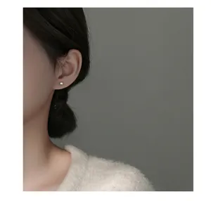 Detailopname van minimalistische zilveren parel oorknopjes gedragen door een model.