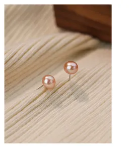 Detailopname van mini roze zoetwaterparel oorbellen op zachte beige gebreide stof achtergrond.
