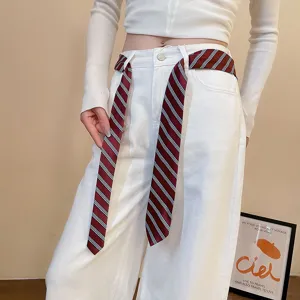 Detail view of a vintage striped silk scarf worn as a stylish waist belt on white trousers.