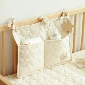 Detailansicht eines cremefarbenen, herzgesteppten Babybett-Organizers an einer Holzreling.