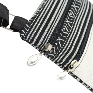 Close-up of black and white striped crossbody bag detail showing dual zippers and metal pulls.