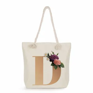 Canvas tote bag detail with large gold letter D and elegant vintage floral graphic.