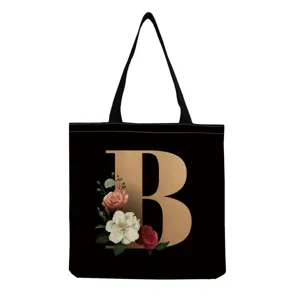 Black canvas tote bag detail featuring a golden letter B and vintage floral print.